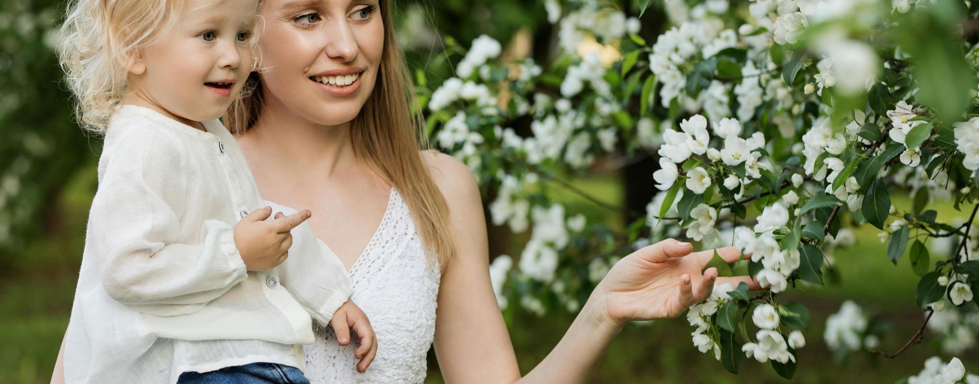 A mother with her young child in a lush orchard full of blooming white flowers, capturing a tender moment.